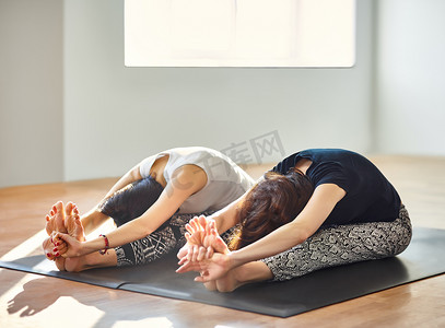 瑜伽体式摄影照片_两个年轻女人做瑜伽体式坐前屈