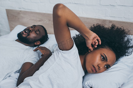选择性的焦点非洲美国妇女用手指堵住耳朵，而躺在打鼾丈夫附近