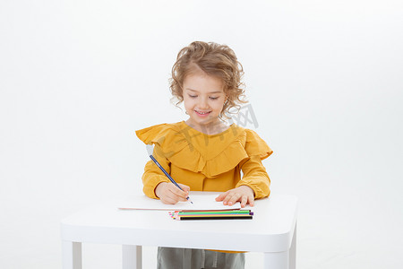 一个可爱的小女孩，拿着铅笔在桌子边画画，铅笔被白色背景隔开了