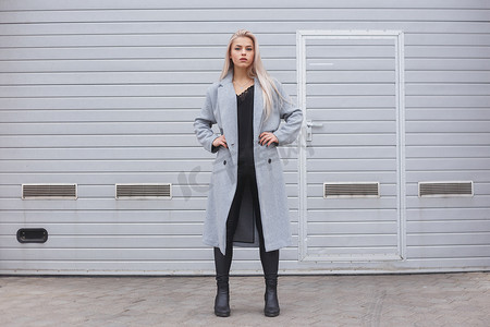 灰色简约墙摄影照片_优雅的年轻女子身穿灰色上衣对抗粗糙的街道墙, 简约的城市服装风格