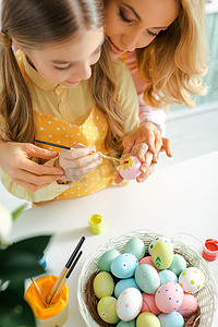 overhead view of kid painting easter egg near mother 