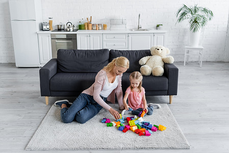eva积木摄影照片_妈妈和孩子在厨房的沙发上玩玩具熊附近的积木
