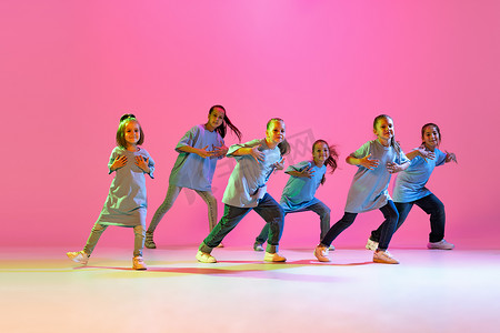 Happy children dancing. Group of children, little girls in sportive casual style clothes dancing in choreography class isolated on orange background in purple neon light. Concept of music, fashion