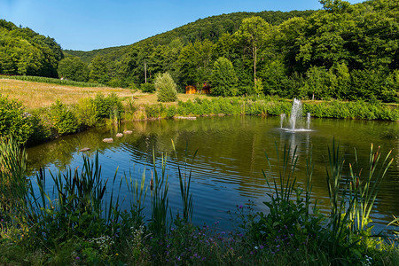 山草坪摄影照片_小喷泉在湖的中间在一个草坪在高绿色山附近