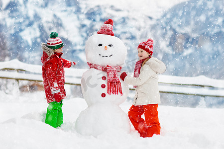 小孩堆雪人孩子们造雪人。在寒冷的冬日，男孩和女孩在户外玩耍。家家户户在山里过圣诞假期很开心.孩子们在瑞士山区玩耍.