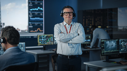 一个快乐的男性飞行管制员在飞行控制中心拍摄相机的肖像。穿着头饰和白衬衫的成功人士。背景下的电脑屏幕.