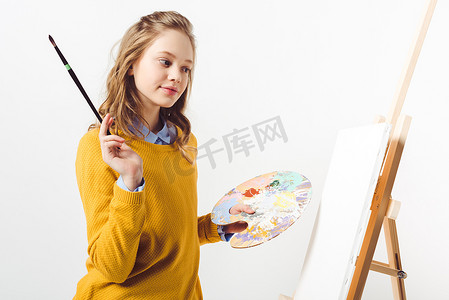 美丽的青年女画家在黄色毛衣与油漆刷子和调色板