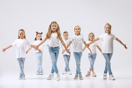 isolated摄影照片_Modern choreography lesson. Dance group of happy, active little girls in jeans and t-shirts dancing isolated on white studio background. Concept of music, fashion, art, childhood, hobby.