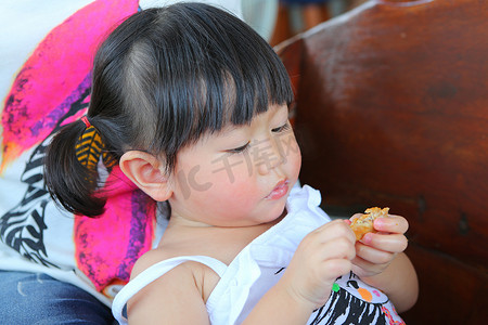 一岁六个月的孩子，小女孩躺在母亲膝上，吃一只鸡翅膀的肖像