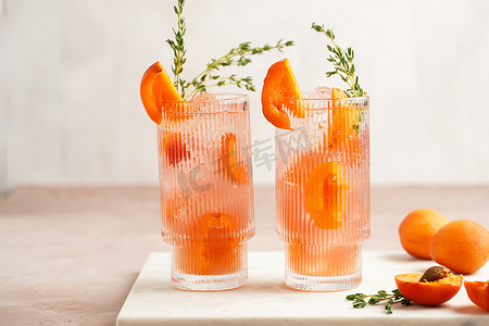 refreshing摄影照片_Two glasses with refreshing summer cocktail with ice cubes, apricot slices and fresh thyme on marble board on pale purple background