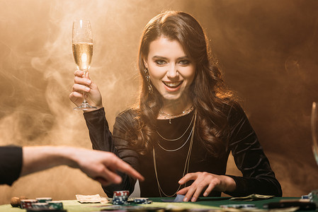 有吸引力的快乐女孩拿着一杯香槟在赌场的扑克桌上, 看着相机