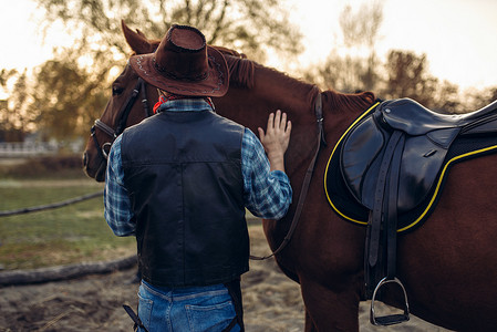 穿着牛仔裤和皮夹克的残酷牛仔在西部的德州牧场与马摆姿势。复古男性人与动物, 狂放的西部