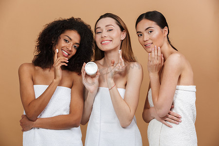 三 smilng 不同类型皮肤的多种族妇女的美照片: 白种人, 非洲裔美国人和亚洲女孩, 在米色背景下涂抹面霜