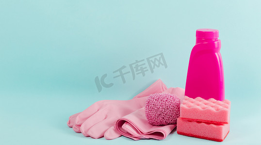 用蓝色底色清洁粉红物料收集.家务劳动的概念。清洁剂、毛巾、橡胶手套、餐巾纸和洗涤剂