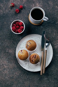 在深色混凝土桌子背景的盘子上喝一杯黑咖啡和覆盆子松饼。顶视图， 平铺， 早餐概念.