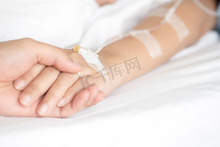 在医院病床上静脉注药治疗男性手牵手接受盐水溶液的选择重点安慰和鼓励他的妻子。医疗、保健.