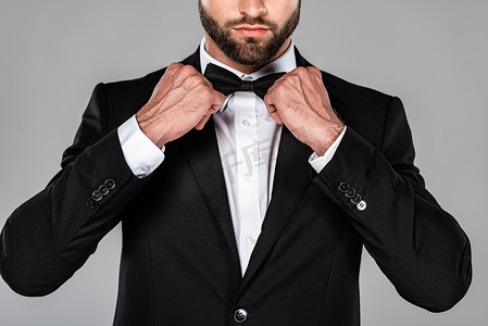 裁剪视图优雅的男人在黑色西装固定领结隔离在灰色
