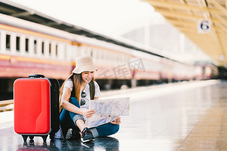 亚洲背包旅行者女人使用泛型的本地地图，独自一人坐在火车车站月台带的行李。夏季假日旅游或年轻旅游概念