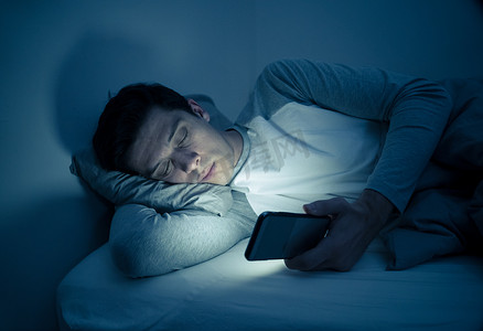 年轻的手机成瘾者晚上在床上醒来, 用智能手机聊天、调情和发短信。在传播、网络成瘾和社交媒体网络滥用概念中