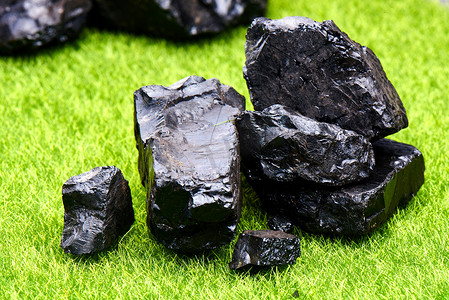 天然煤在绿色草坪背景隔离特写镜头。天然矿产资源的提取.