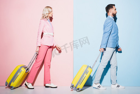 外景迷人的女人和英俊的男人背着粉色和蓝色背景的旅行包走在一起 