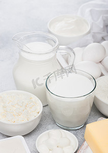 白色桌子背景的新鲜乳制品。罐和一杯牛奶, 一碗酸奶油, 奶酪和烤面粉和马苏瑞拉。鸡蛋和奶酪. 
