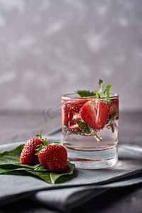 饮料夏季摄影照片_用草莓和薄荷糖在灰色餐巾纸上的闪闪发光的玻璃杯在混凝土桌子上的水，复制空间。寒冷的夏季饮料。矿泉水