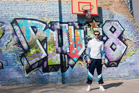 涂鸦篮球摄影照片_时尚的年轻男子在老式服装在砖墙前的涂鸦和篮球戒指