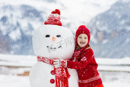 冬日限定摄影照片_小孩堆雪人孩子们造雪人。在寒冷的冬日，男孩和女孩在户外玩耍。家家户户在山里过圣诞假期很开心.孩子们在瑞士山区玩耍.