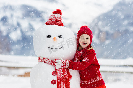 小孩堆雪人孩子们造雪人。在寒冷的冬日，男孩和女孩在户外玩耍。家家户户在山里过圣诞假期很开心.孩子们在瑞士山区玩耍.