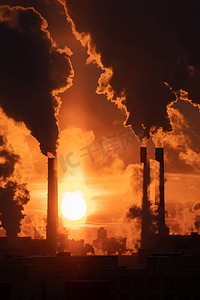 二氧化碳排放摄影照片_在红色落日的天空下，燃煤发电厂的烟囱冒着烟。冬季城市的空气污染