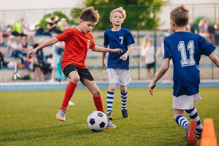 足球比赛字体设计摄影照片_男孩子们在踢足球。青少年足球队之间的训练和足球比赛。球员之间的初级比赛:跑动和踢足球.儿童足球锦标赛的最后一场比赛