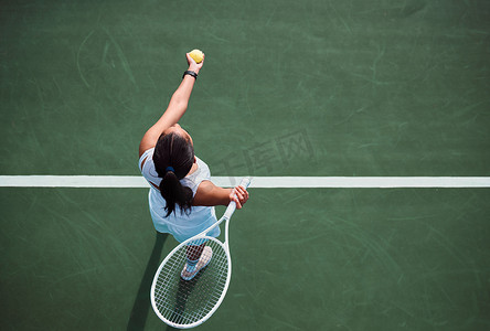 High angle shot of a young woman serving a ball while playing tennis on a court.