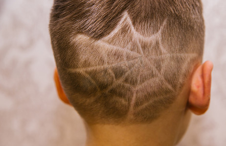 The spider-Man symbol is shaved by a clipper on a child's head. Drawing of a haircut on the boy's head in the form of a web.Stylish and fashionable hairstyle.