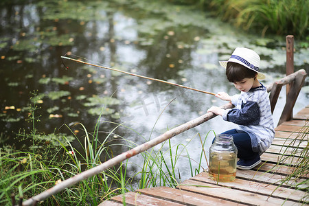 钓竿折断摄影照片_秋天的早晨，一个孩子在钓鱼。秋天的落日落在池塘上.一个在人行道上拿着钓竿的渔夫.