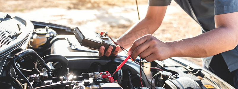 中值摄影照片_机械修理工检查发动机汽车在汽车维修服务中的应用，用数字万用表测试电池测量各种值并进行分析.
