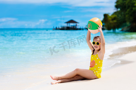 小孩玩水摄影照片_孩子们在热带海滩打球。在海滨的小女孩。家庭暑假。孩子们玩水沙玩具。海洋和岛屿的乐趣。和小孩一起旅行亚洲假日.