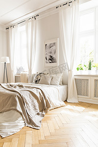 米色毯子在床和海报在白色卧室内部与窗帘在窗口。真实照片