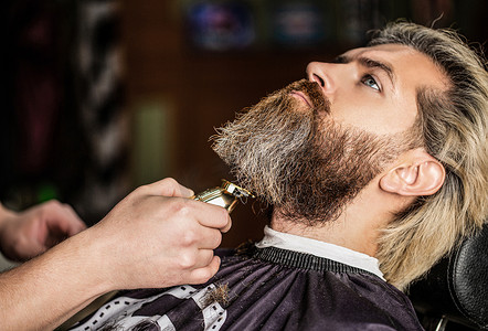 理发师带着胡子钳工作.Hipster的客户正在理发有胡子剪子的理发师的手，特写。理发店里有胡子的男人在理发店拜访理发师的男人