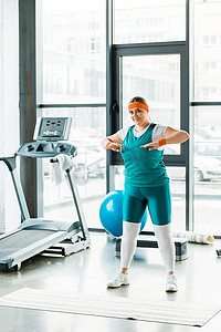 运动健身垫摄影照片_超重的妇女伸展, 而站在运动服装附近的健身垫