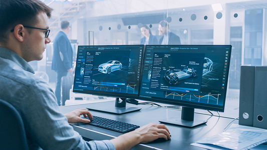 专业工程师使用 3d Cad 软件在计算机上工作，并在高科技开发实验室中测试电动汽车底盘原型，并配有车轮、电池和发动机.