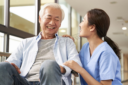 nursing摄影照片_young friendly asian female caregiver talking to elderly man in 