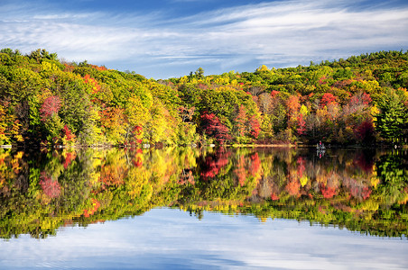 秋天的艳阳天，康涅狄格州托林顿伯尔州立公园的五彩缤纷的秋树在水面上反射着光芒.