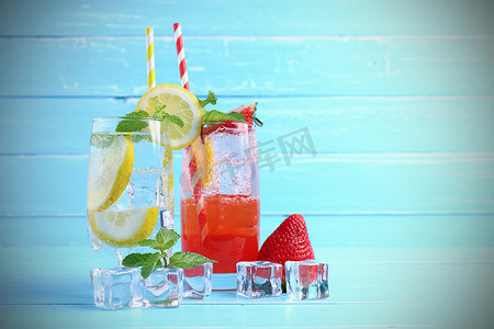 柠檬汁和草莓汁混合苏打水，不含酒精，玻璃杯装饰薄荷叶，切碎石灰在蓝色木制桌子上，并留有复制空间。夏季酒水的概念.