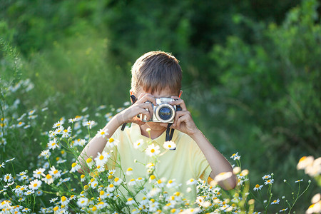 花地摄影照片_带着专业相机的孩子们正在阳光灿烂的夏日拍摄大自然的花朵。小孩在迷迭香花地拍照.