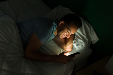 兴奋的年轻人一边在智能手机上发短信，一边看在线视频，同时熬夜