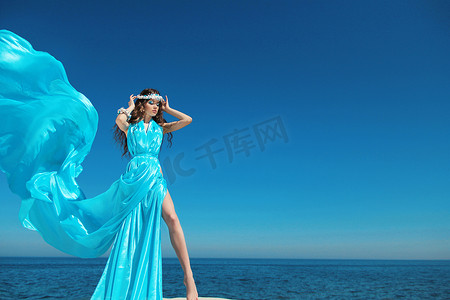 享受。在蓝蓝的天空吹裙子的时尚模型女人,