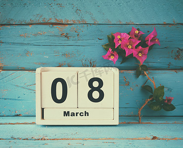 木制的 3 月 8 日日历，旁边旧蓝色仿古桌上紫色的花。选择性的焦点.