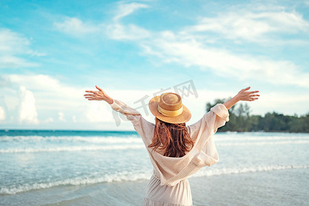 Summer beach vacation concept, Young woman with hat relaxing with her arms raised to her head enjoying looking view of beach ocean on hot summer day, copy space.