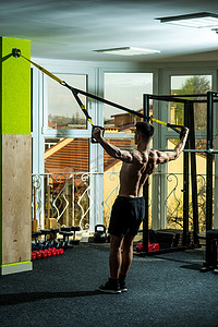 男子与裸躯干, 肌肉背部在健身房享受训练, trx。体育和健身房的概念。人与躯干, 运动员, 运动员, 肌肉男子汉做锻炼与 trx 循环, 窗口在背景上